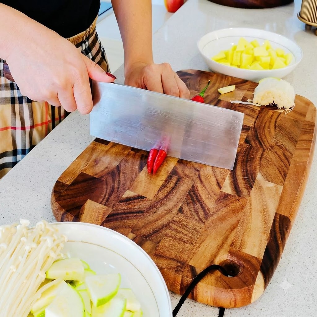 Small red chili peppers being chopped into fine pieces on a wooden cutting board.