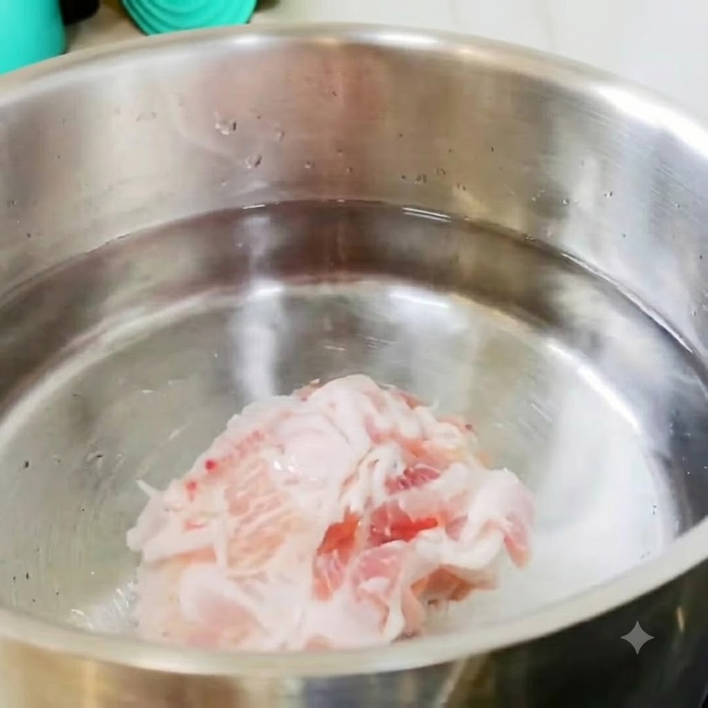 Sliced pork belly and potato pieces resting in a stainless steel pot of cold water on the stove.