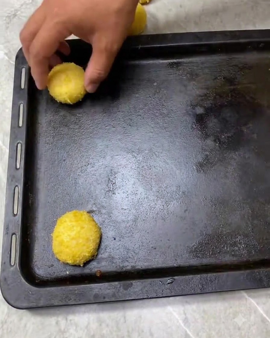Breadcrumb-coated dough balls neatly spaced on a dark baking tray, ready for proofing.