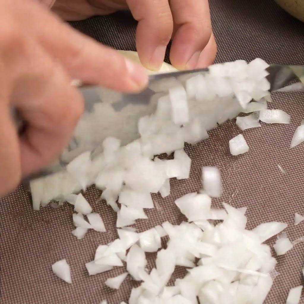 A bowl containing minced beef and pork with finely diced white onions being poured on top.