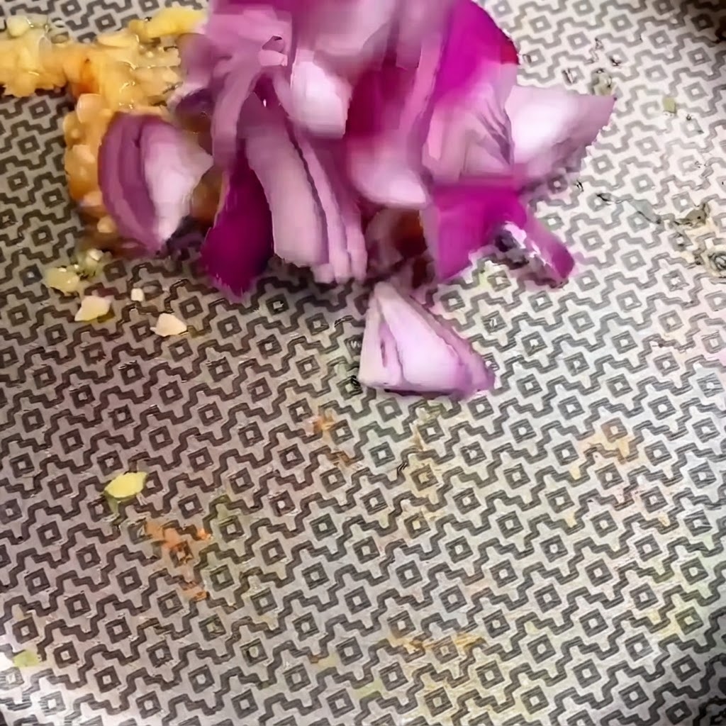 Chopped red onion pieces being added to minced garlic in a patterned pan.