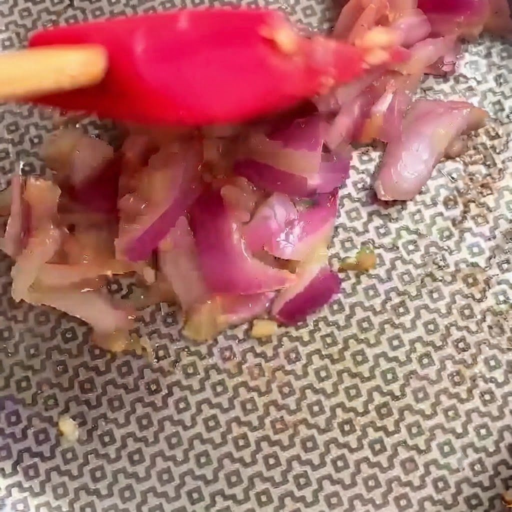 Red spatula actively mixing ingredients inside the cooking pan.
