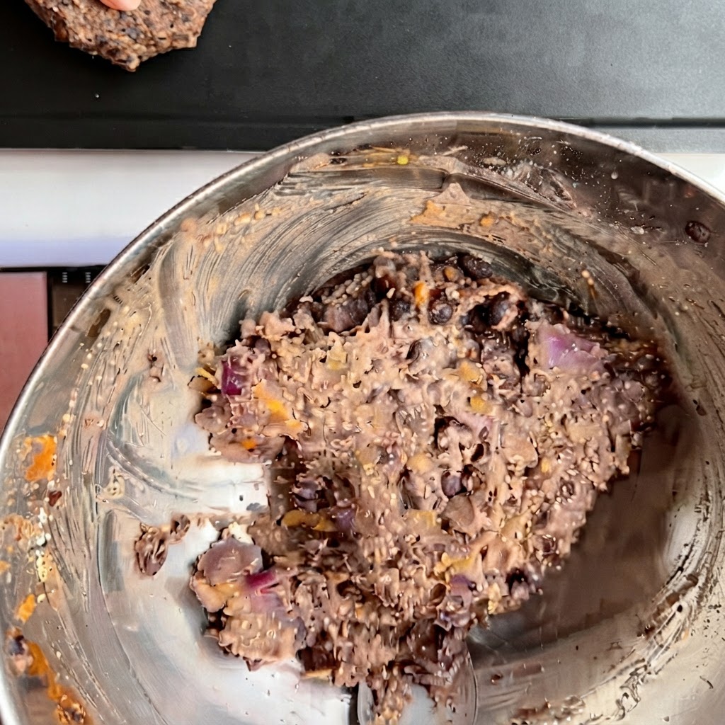 Several shaped black bean burger patties arranged neatly on a dark baking tray.