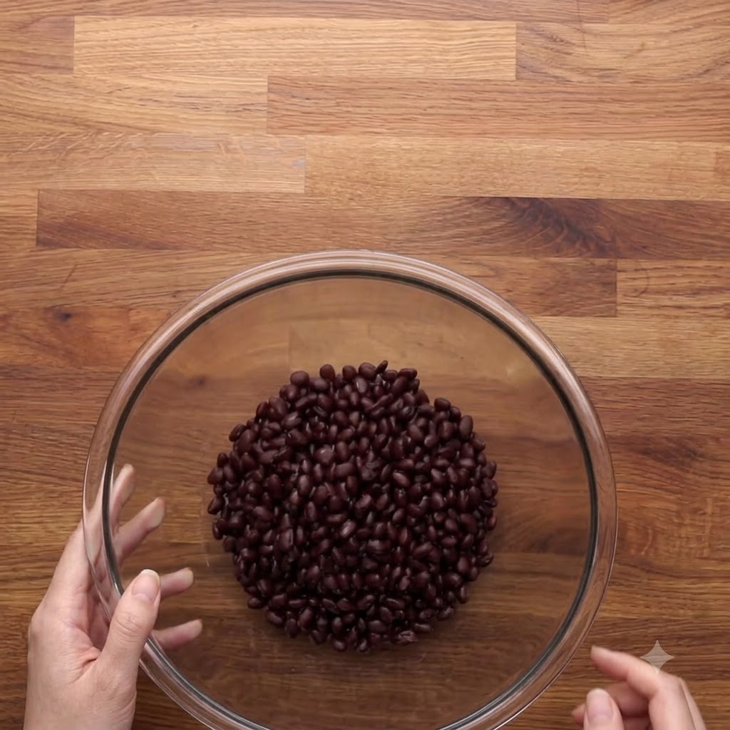 Rinsed and drained black beans sitting inside a large transparent glass bowl on a wooden surface.