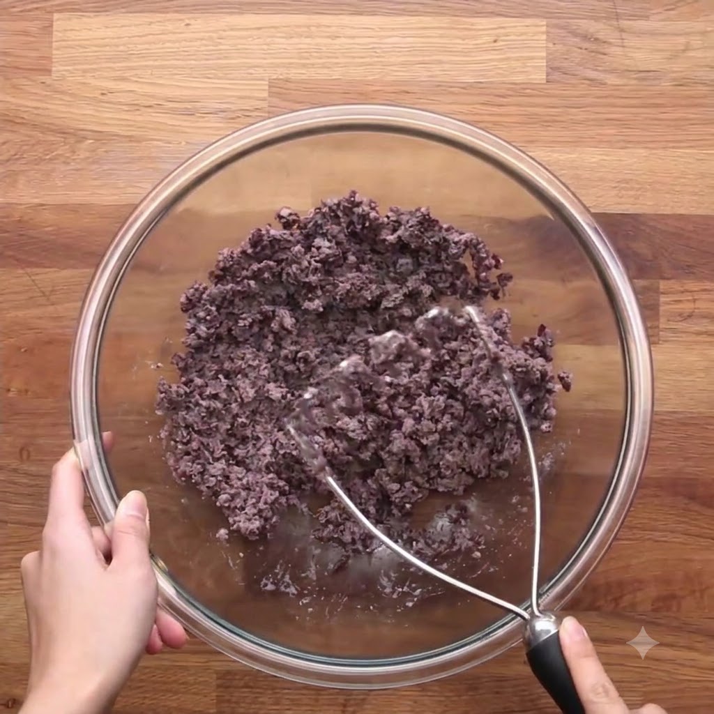 The cooked onion and carrot mixture combined with the mashed black beans in a glass bowl.
