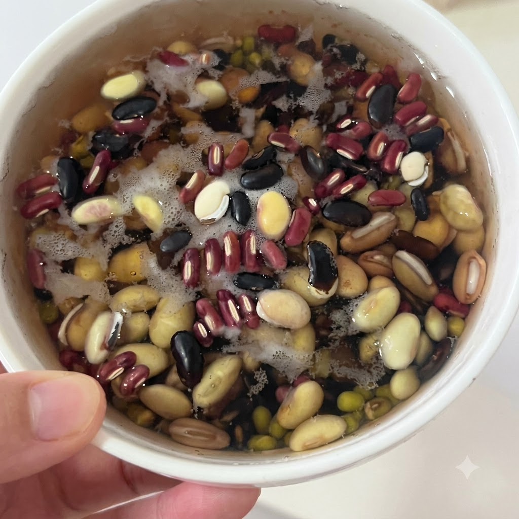 Soaked mixed beans resting in a white bowl with water before being strained.