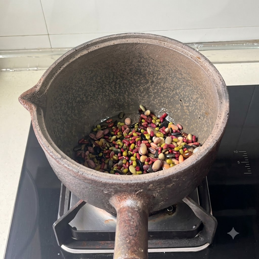 Mixed beans sitting at the bottom of an earthenware cooking pot after water has been added.