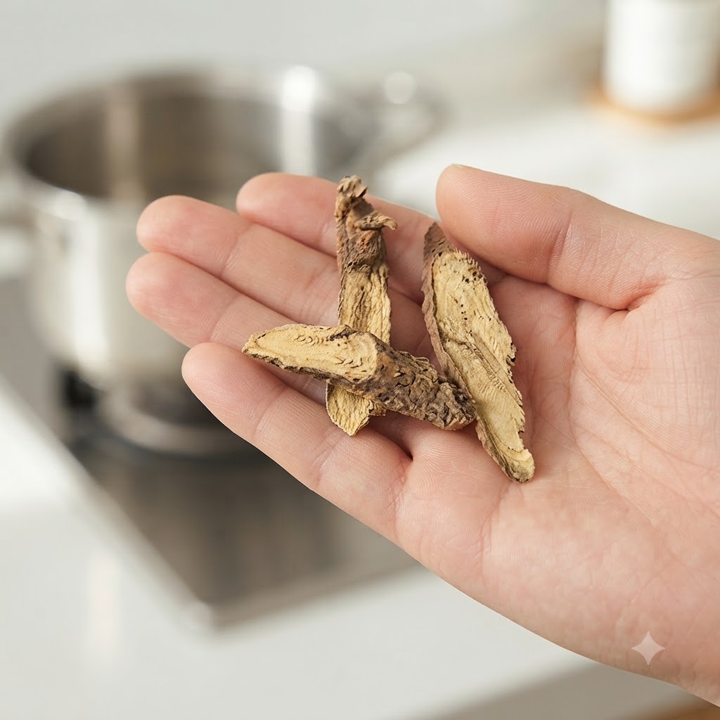 Pieces of dried licorice root being held in a persons hand with an earthenware pot visible in the blurred background.