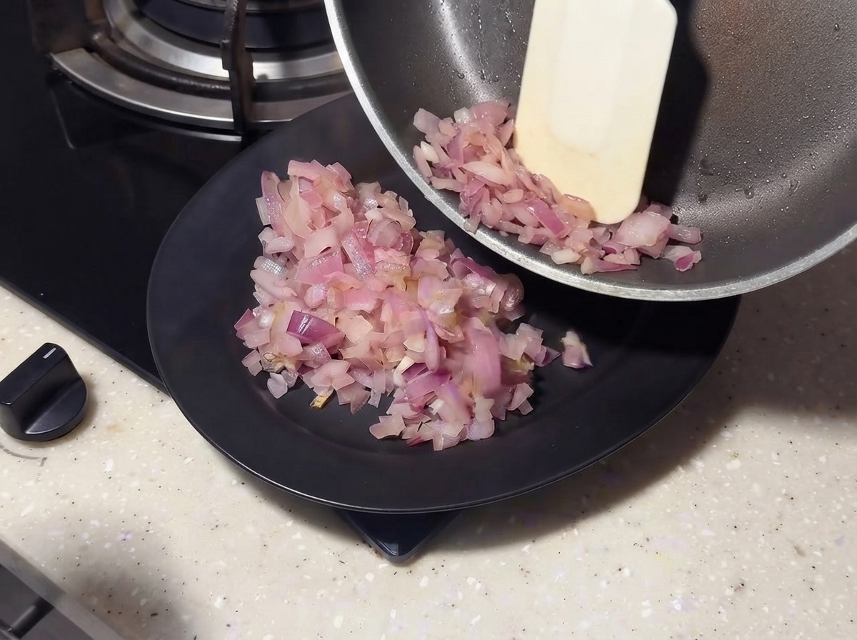 Sautéed onions being slid from a pan onto a black plate using a spatula.