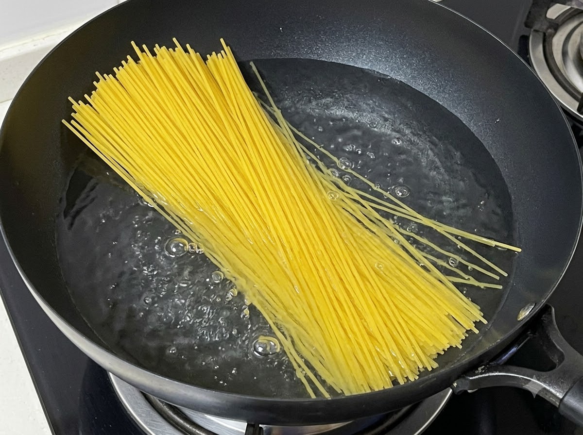 A bundle of dry spaghetti noodles being lowered into a pot of boiling water.