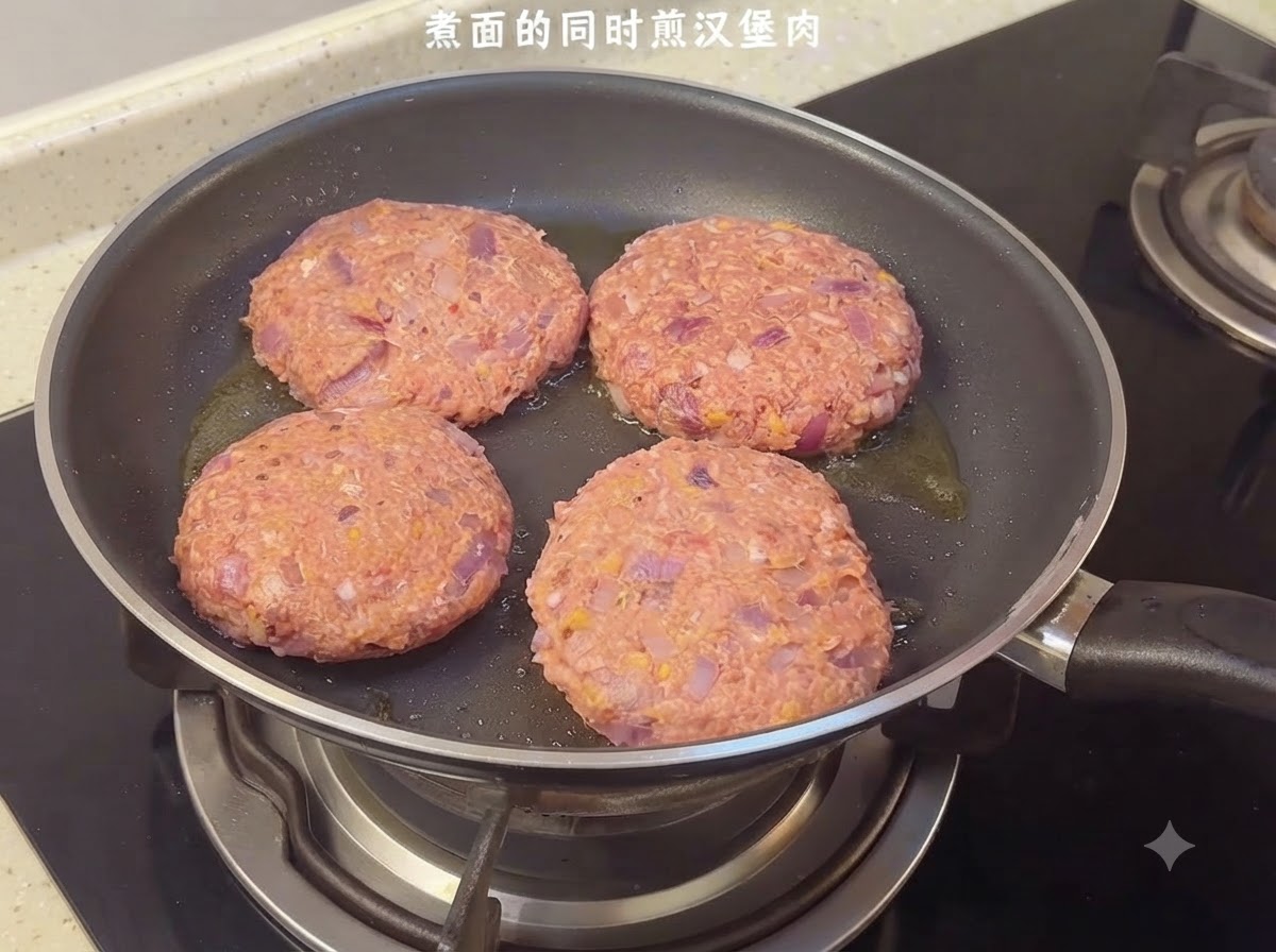 Four raw hamburger patties sizzling in a frying pan on the stovetop.