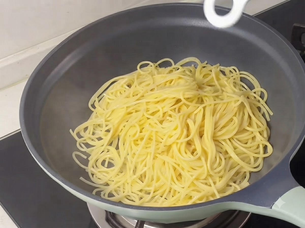 Cooked yellow spaghetti strands piled inside a skillet.