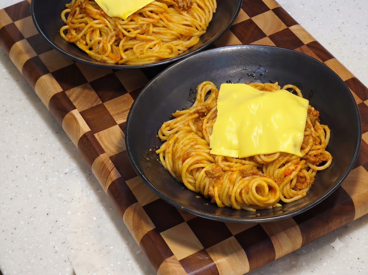 A yellow slice of cheese melting over the spaghetti base inside a black serving bowl.