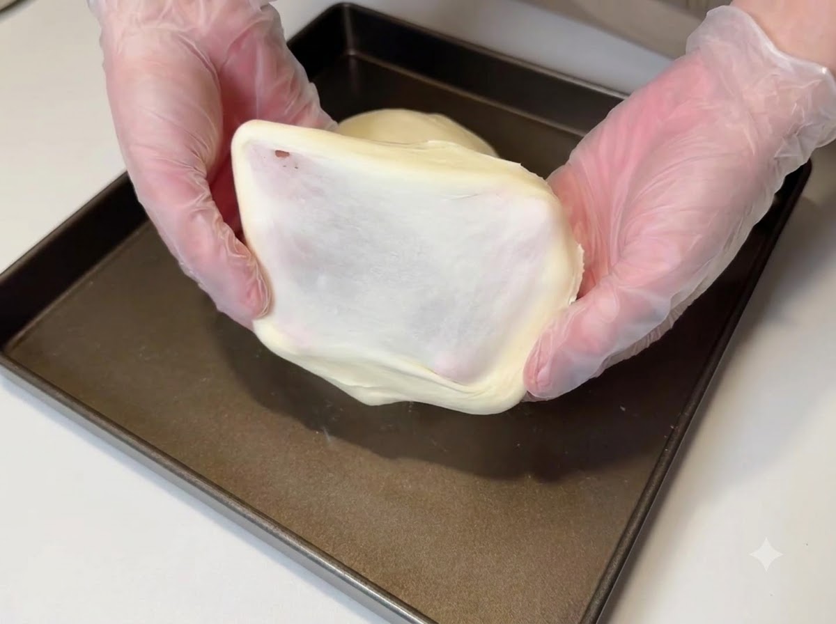 A piece of dough being stretched to show a thick, smooth film.