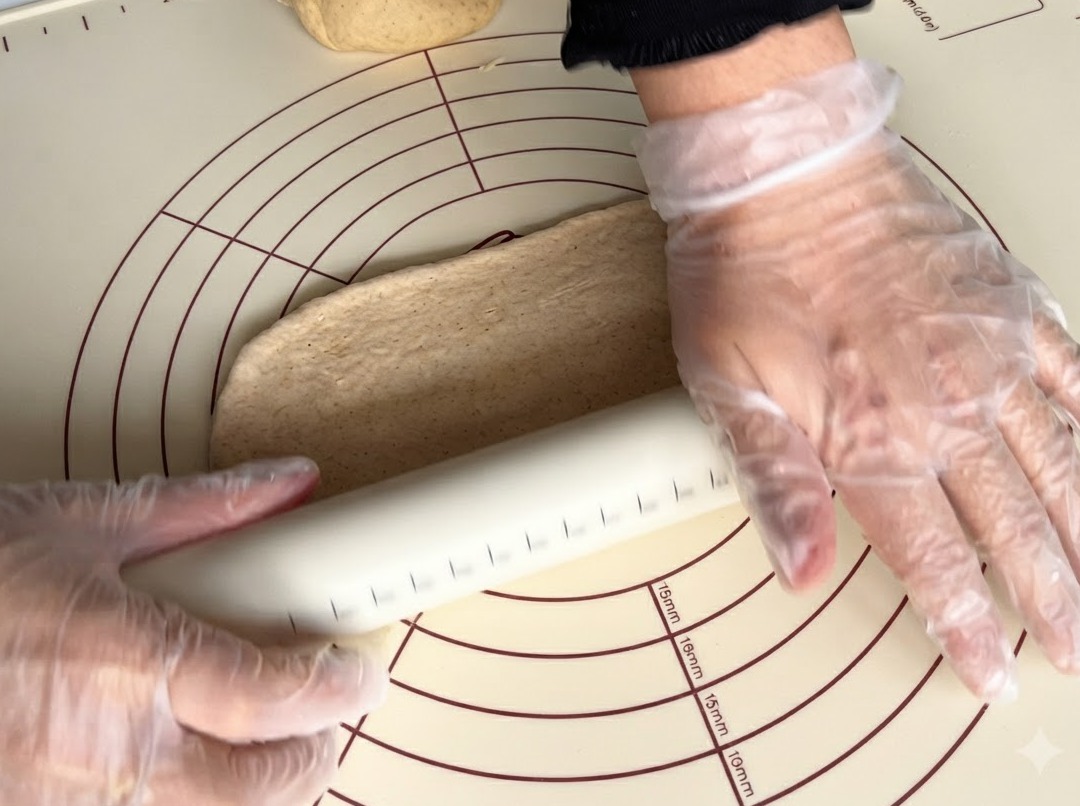A rolling pin flattening a piece of whole wheat dough on a silicone mat.