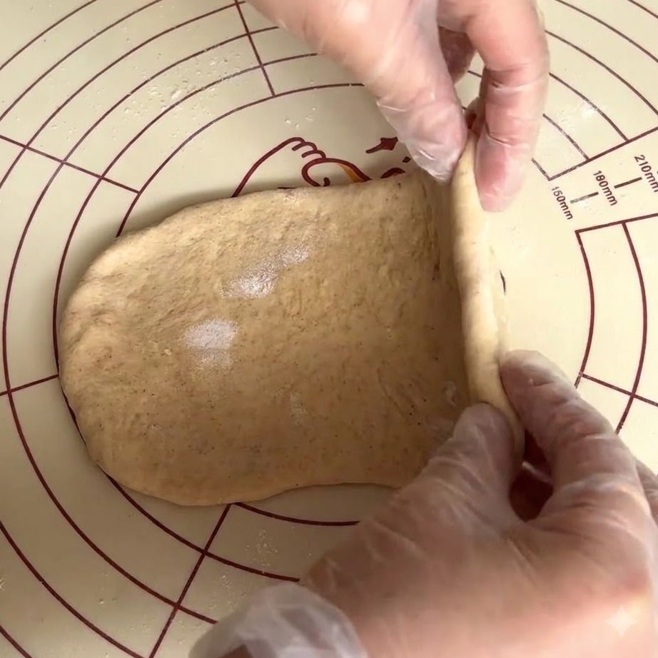 Gloved hands folding and pinching flattened whole wheat dough like a quilt.