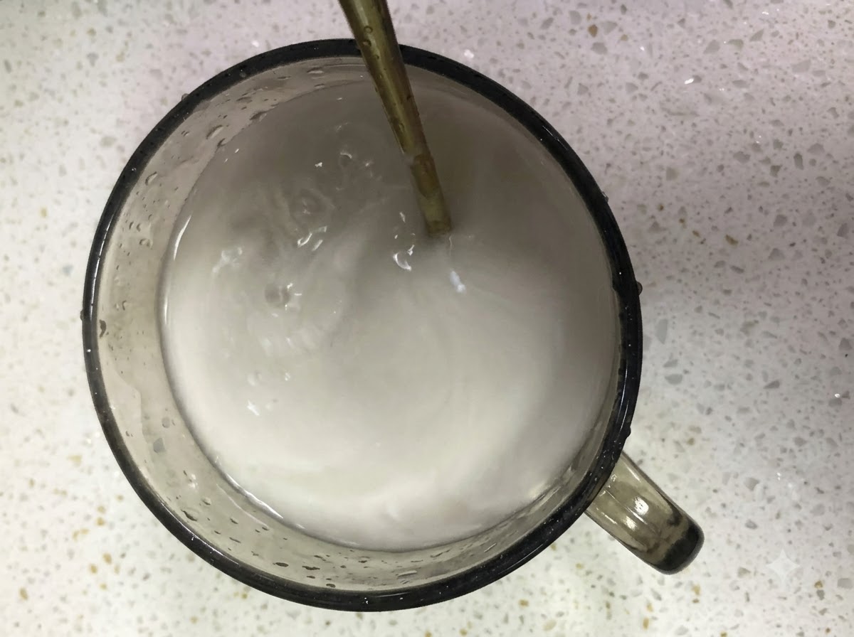 Sweet potato starch and water mixture being stirred in a glass cup with a spoon.
