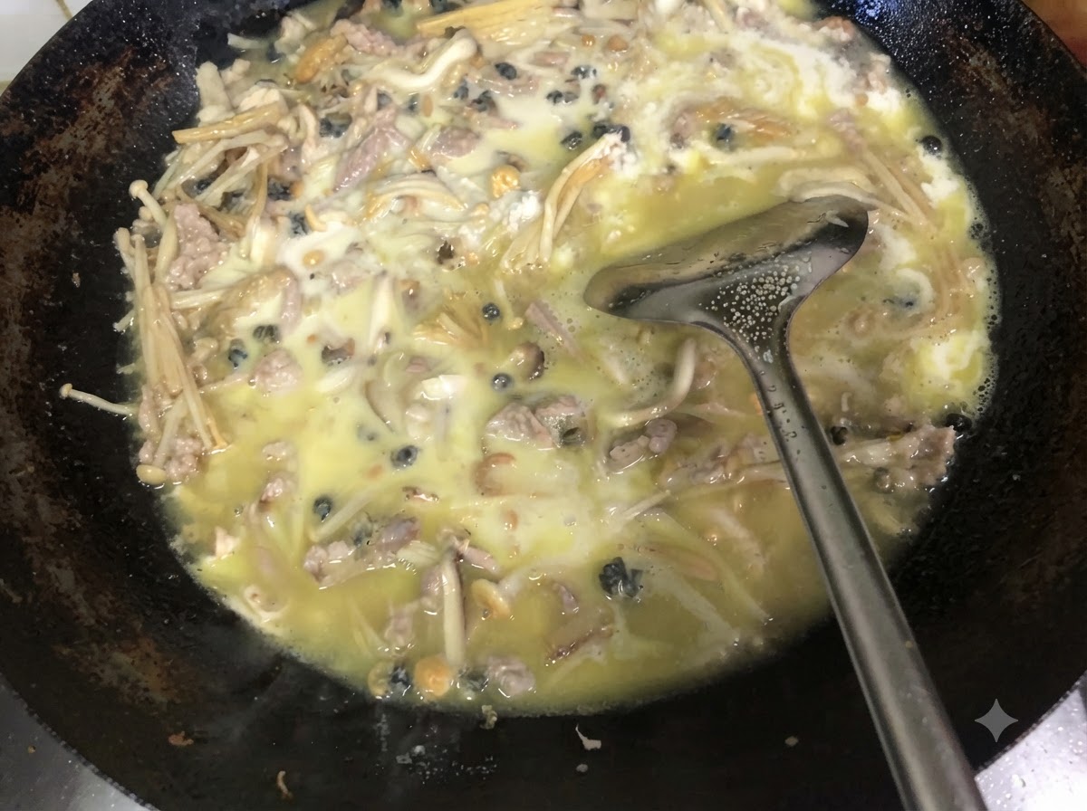 Fresh chopped green chives being mixed into the thick cooked filling inside a wok using a metal spatula.