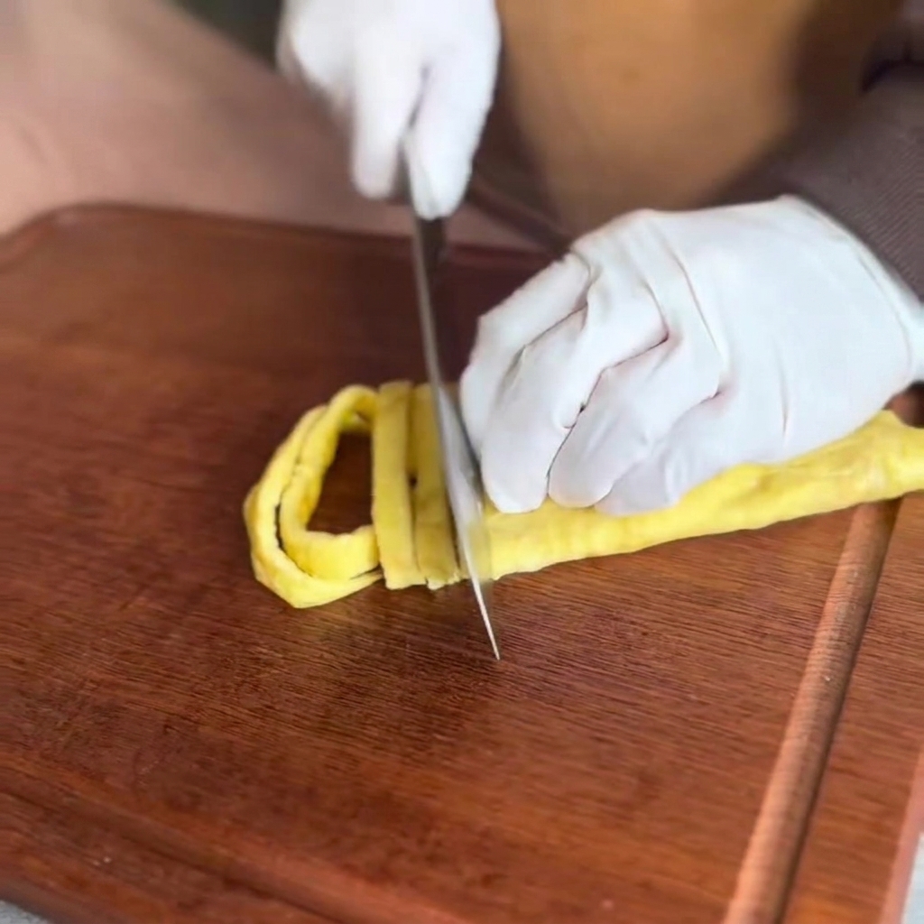 The cooked egg pancake being sliced into fine strips on a wooden cutting board.