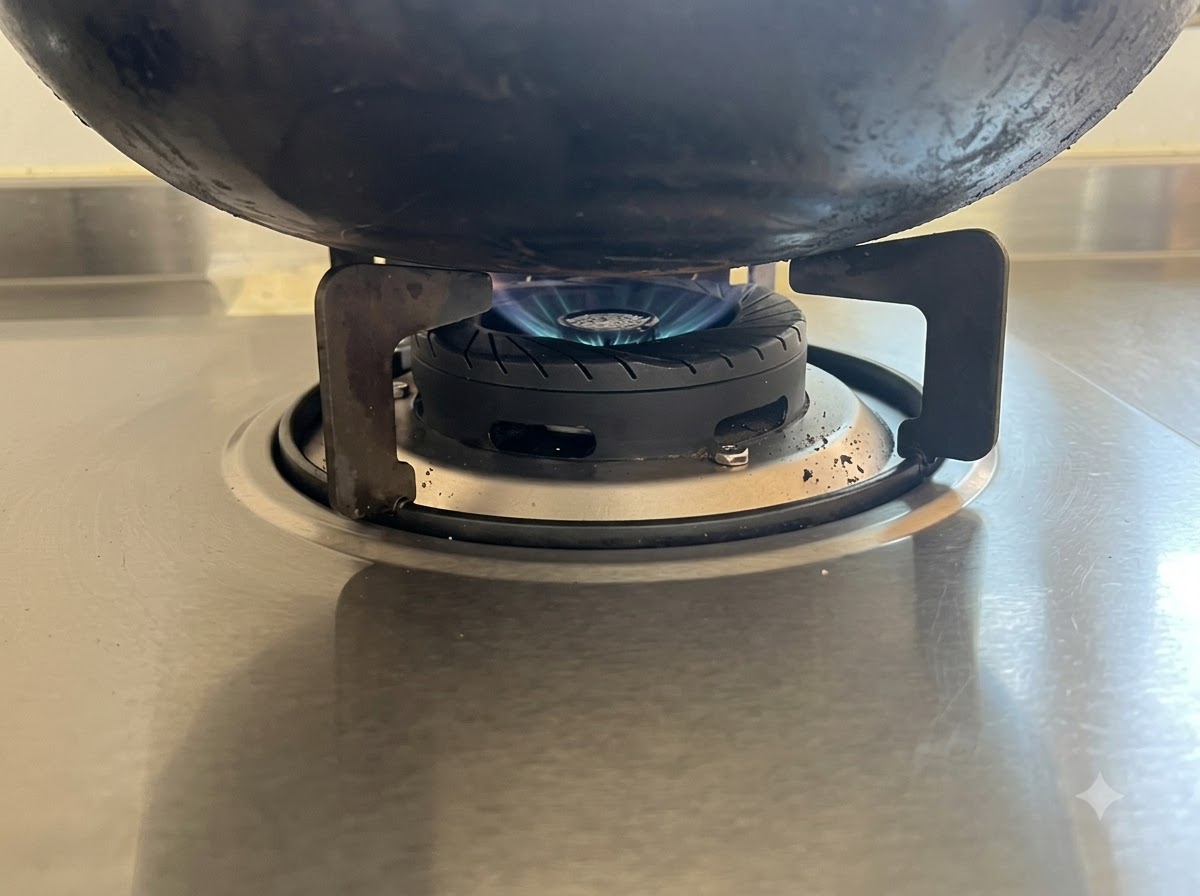 A low blue flame heating the bottom of a black wok on a stainless steel stovetop.