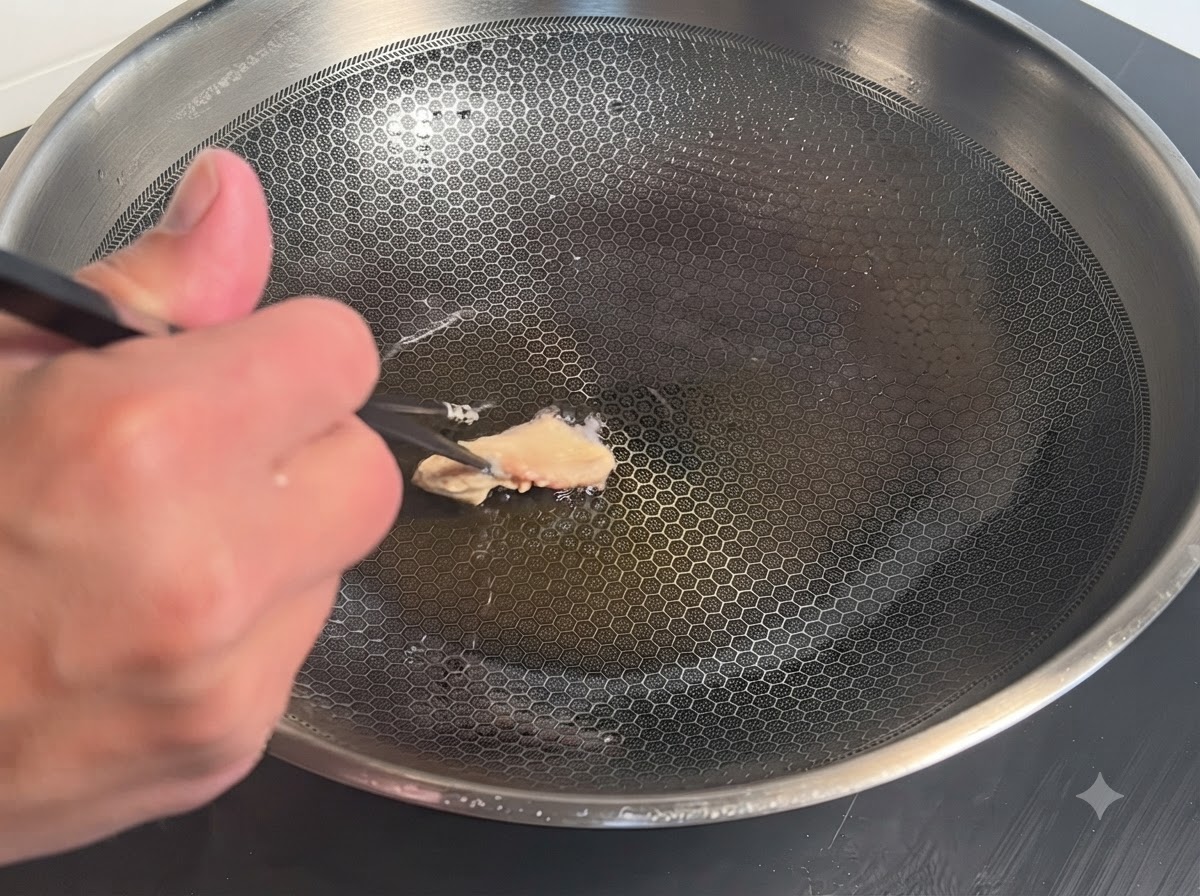 A single piece of batter-coated chicken being placed with chopsticks into a hot metal wok with oil.