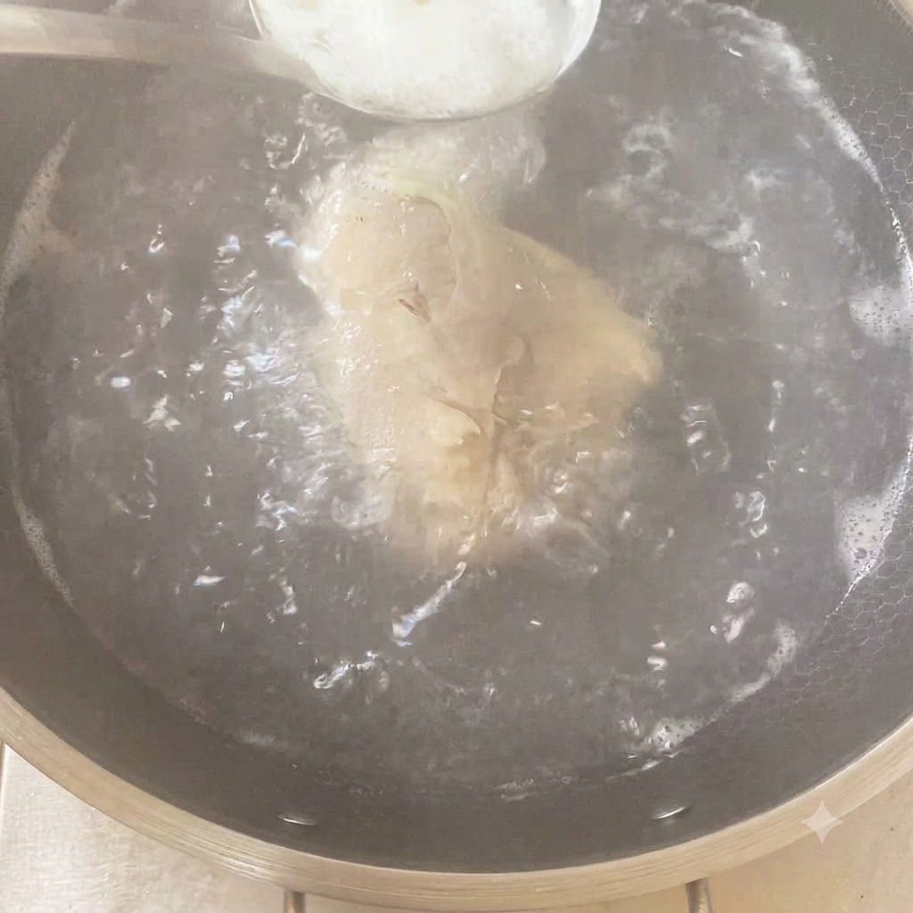 A spoonful of seasoning being added into a boiling pot containing the chicken and aromatics.
