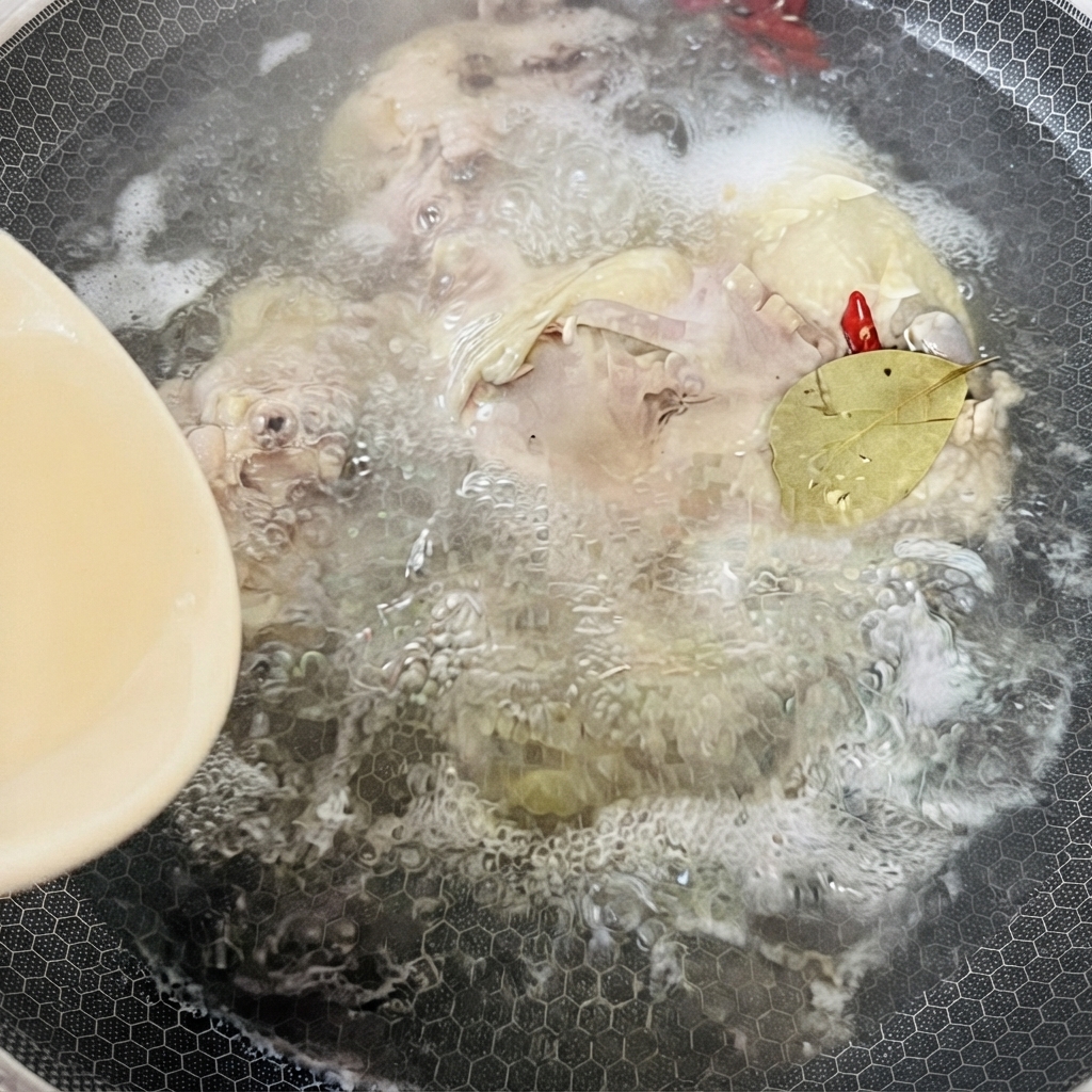 A pot filled with boiling chicken broth, spices, and a bay leaf simmering under heat.