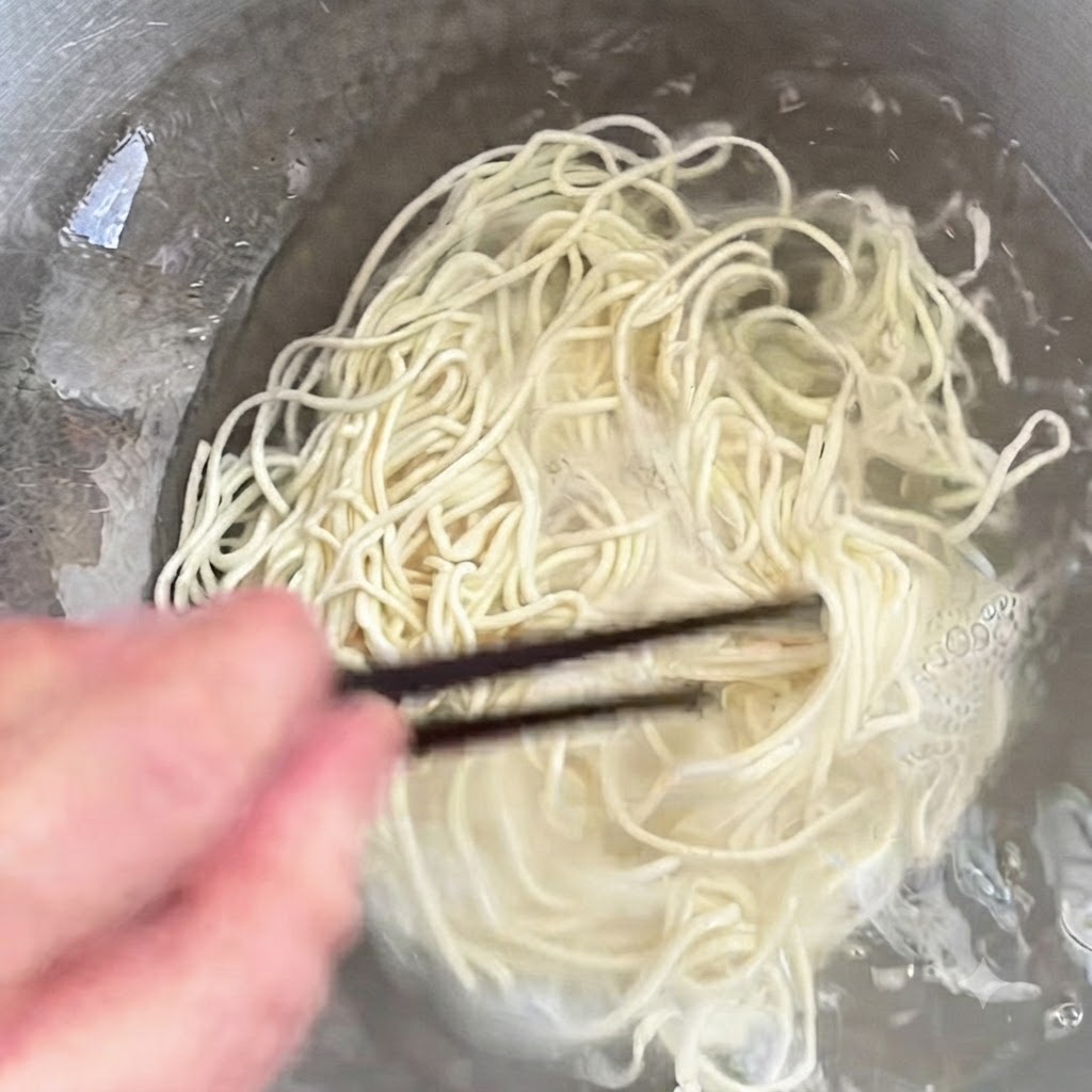 Noodles cooking in a pot being stirred with chopsticks.