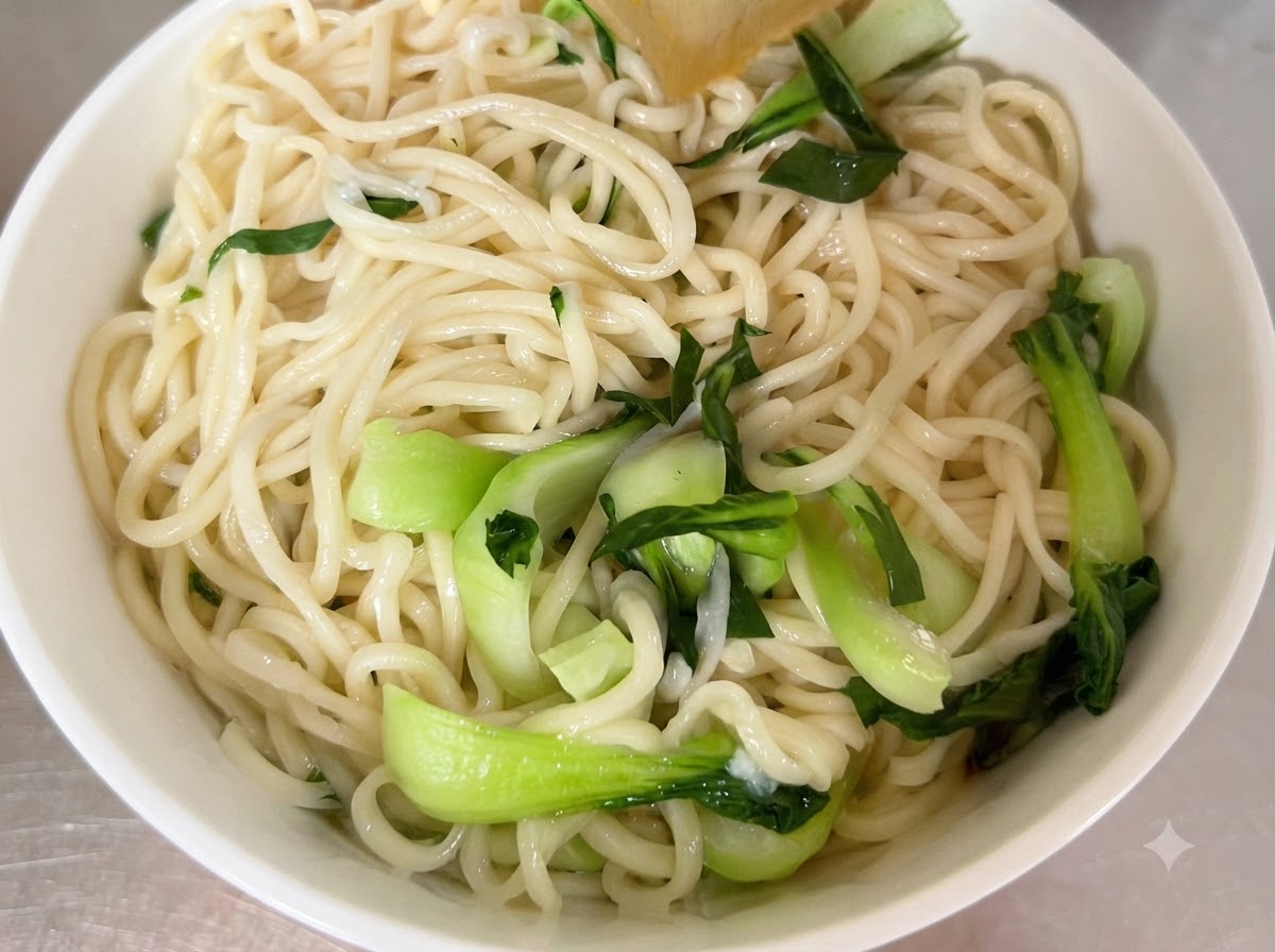 Cooked noodles and fresh bok choy arranged inside a white serving bowl.