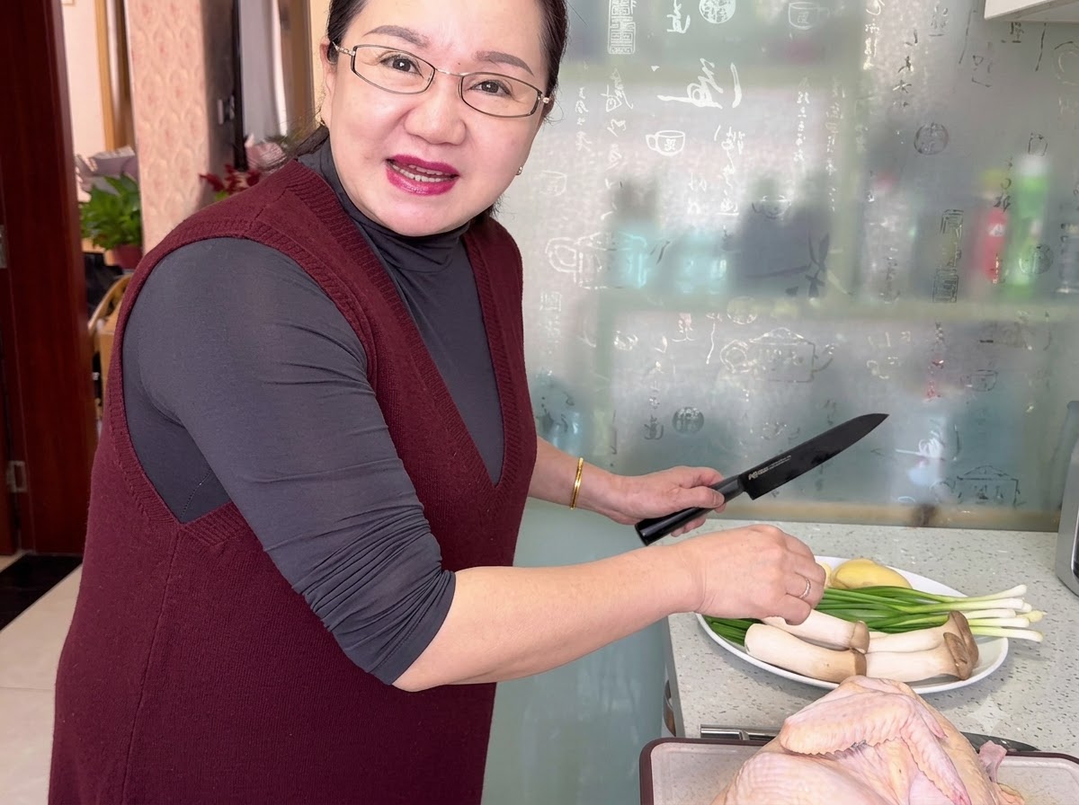 A raw whole chicken being trimmed on a cutting board with a knife.