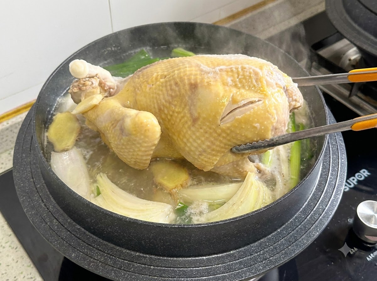 Cooking tongs gripping and turning a whole chicken inside a boiling pot of broth.