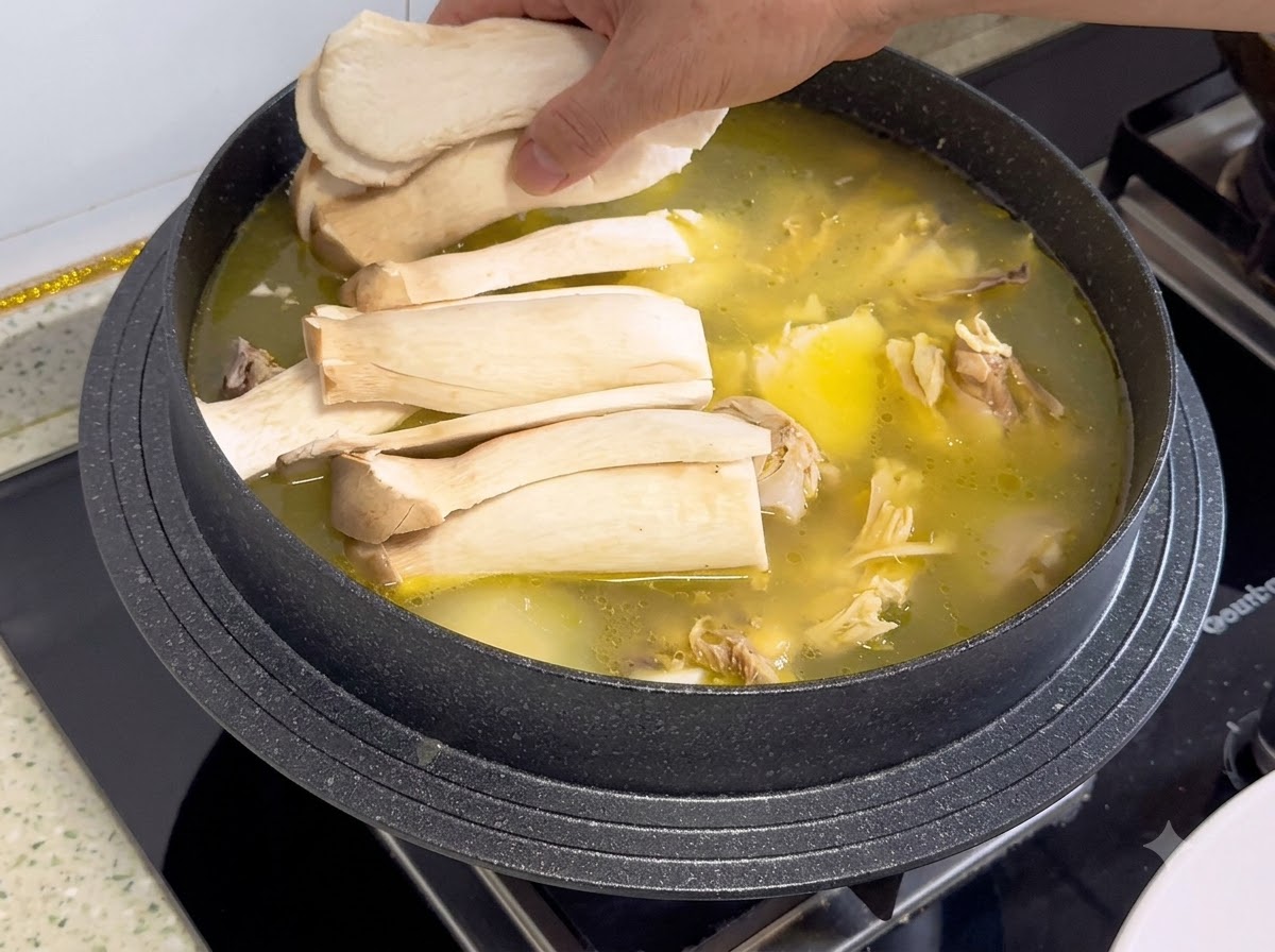 Sliced king oyster mushrooms being arranged on top of the chicken broth and ingredients in a pot.
