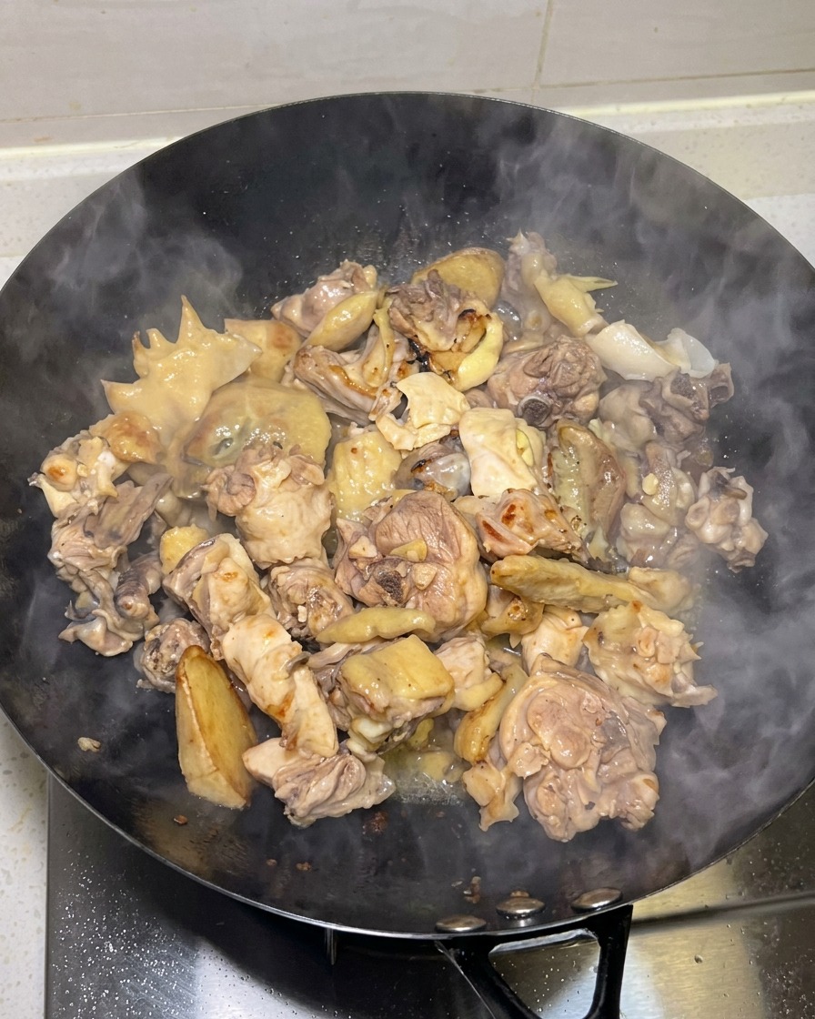 Golden seared chicken pieces being cooked in a wok with steam rising.