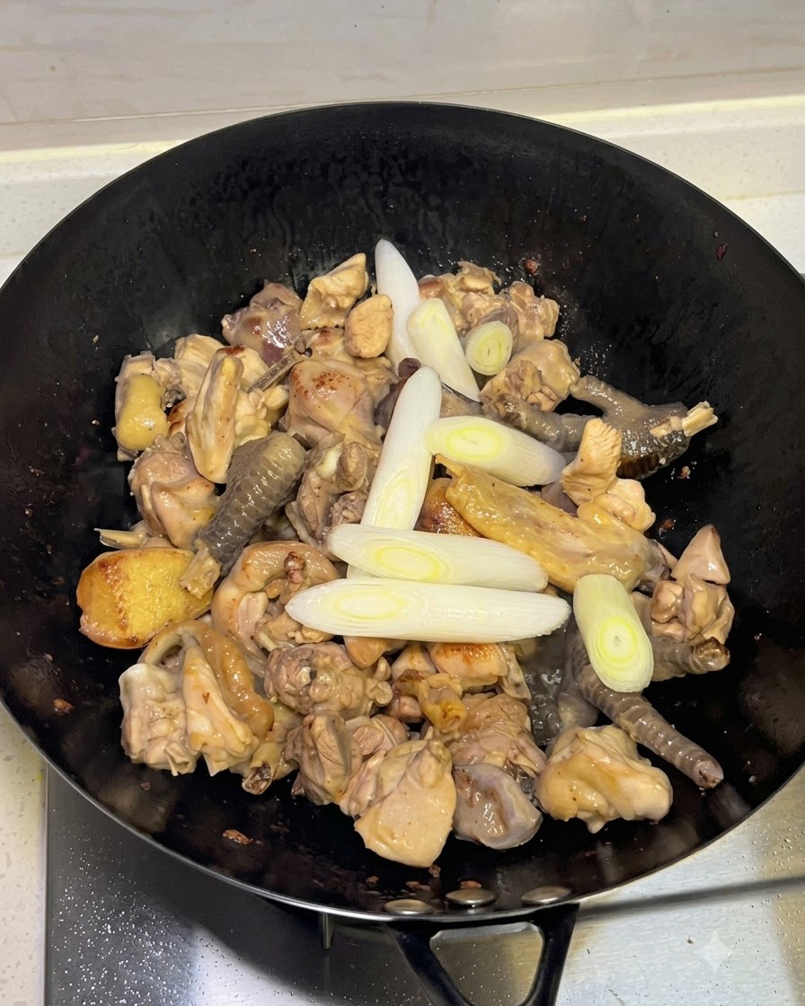 Adding scallions, garlic, and whole spices into the wok with the chicken.