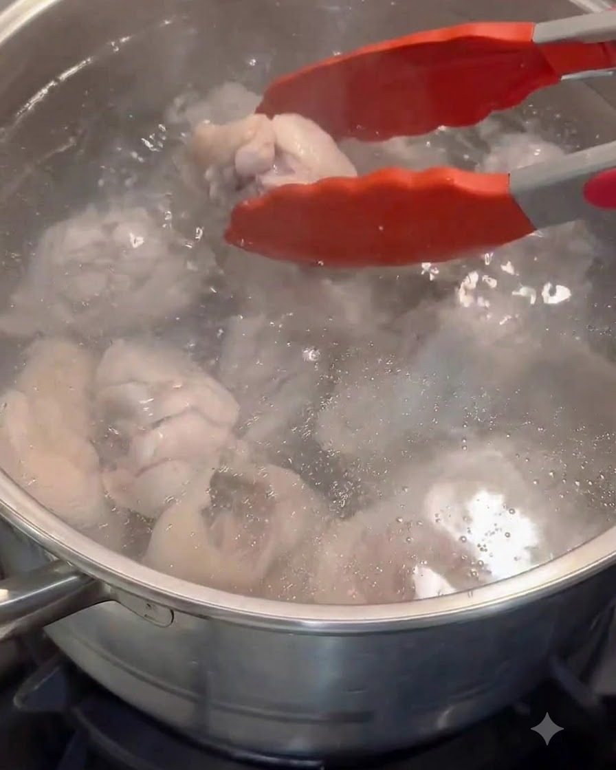 Red tongs transferring blanched chicken pieces into a pot of fresh hot water.