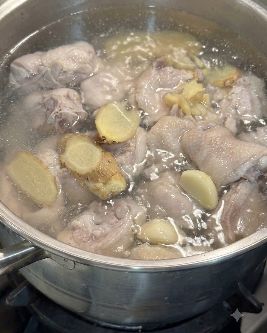 Garlic cloves and ginger slices floating in the pot with chicken pieces in simmering water.