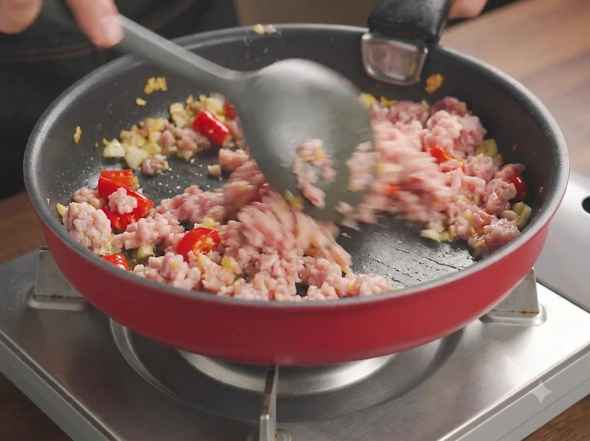 Minced pork being vigorously broken apart and stir-fried with chilies and garlic in a pan.