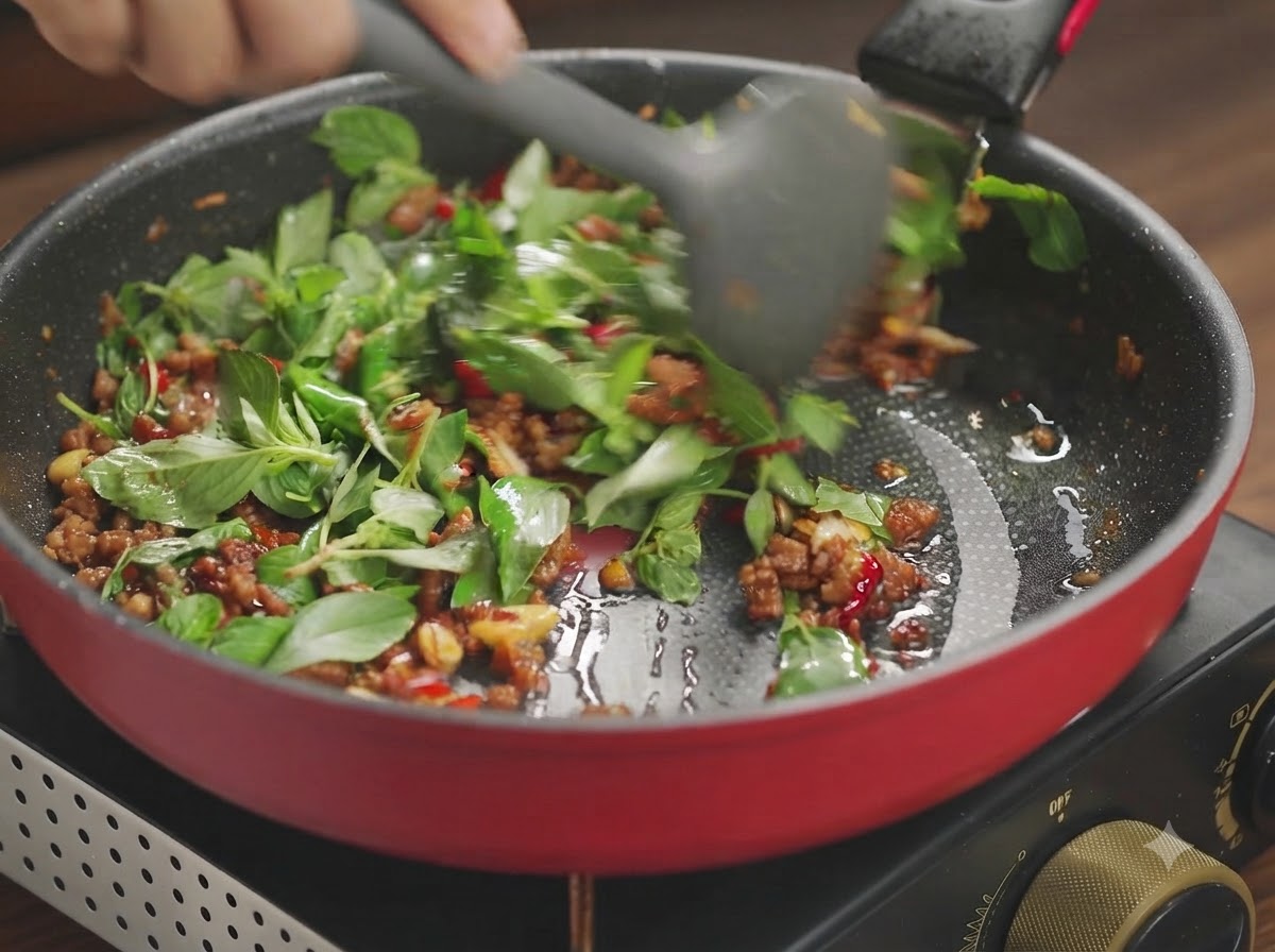 Basil leaves and minced pork being toss-fried together until the greens are wilted.