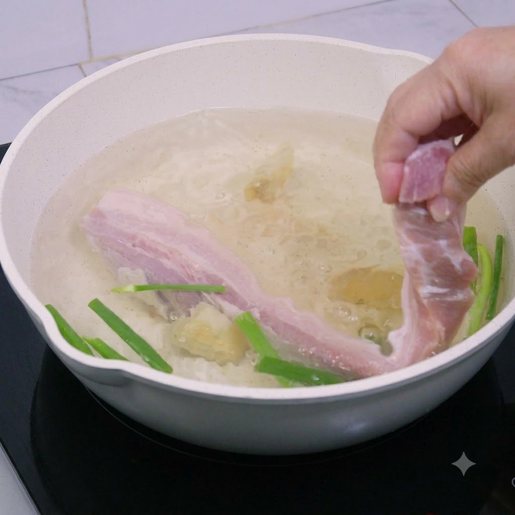 Pork belly strips being lowered into a pot of boiling water.