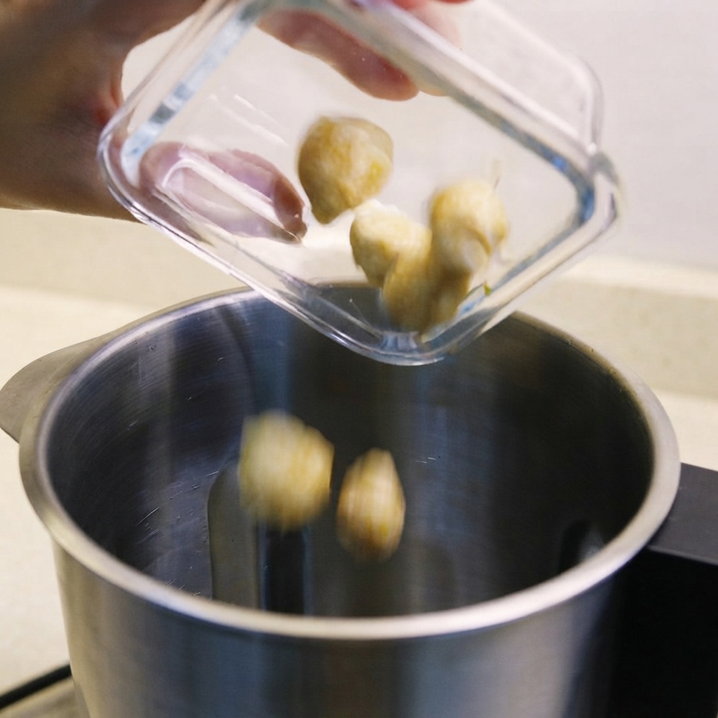 Candlenuts, shallots, and sautéed belacan being poured into a blender container.