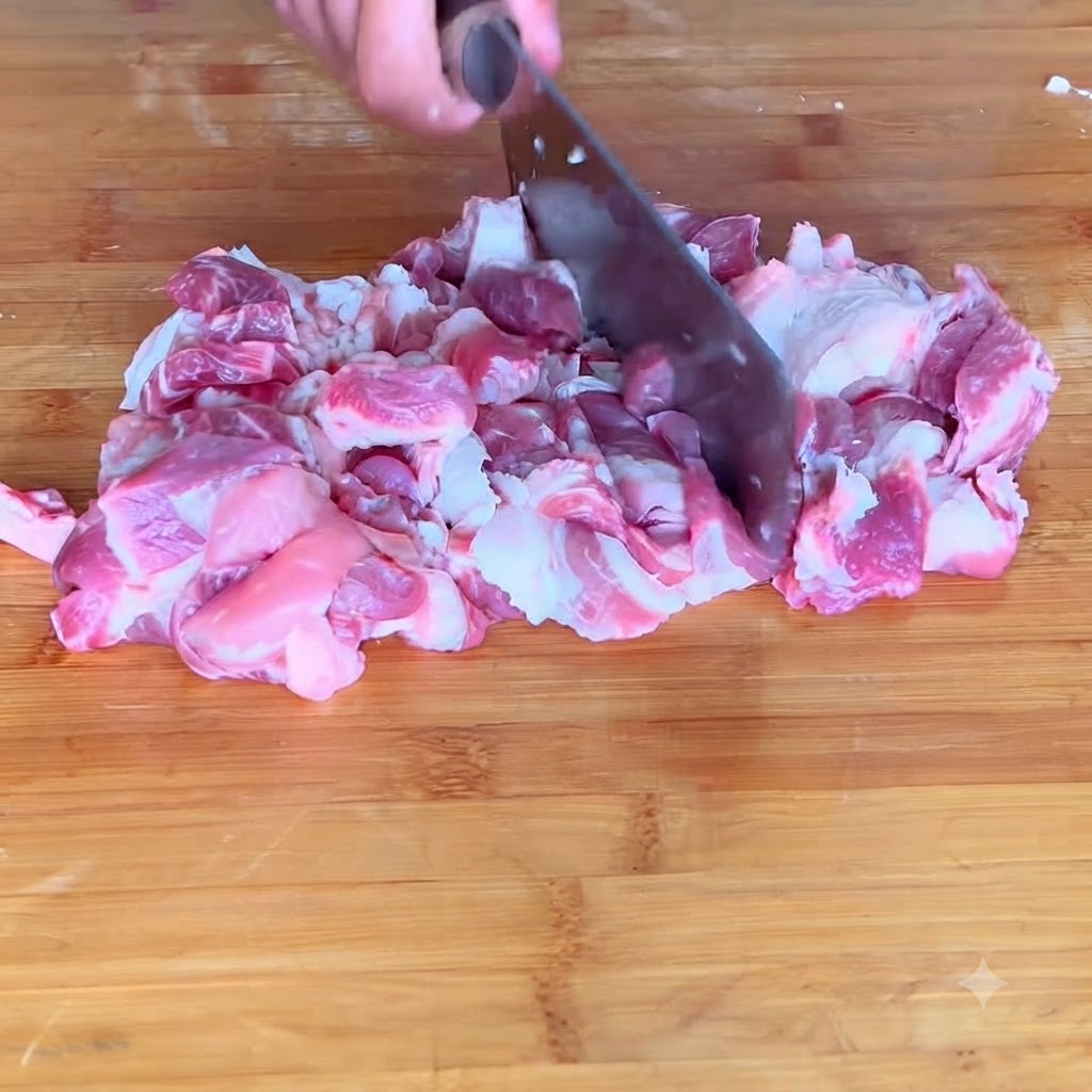 Close-up of pork being chopped into fine meat paste on a cutting board.