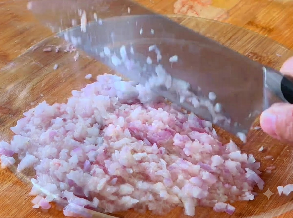 An onion being diced into small pieces on a cutting board with a cleaver.