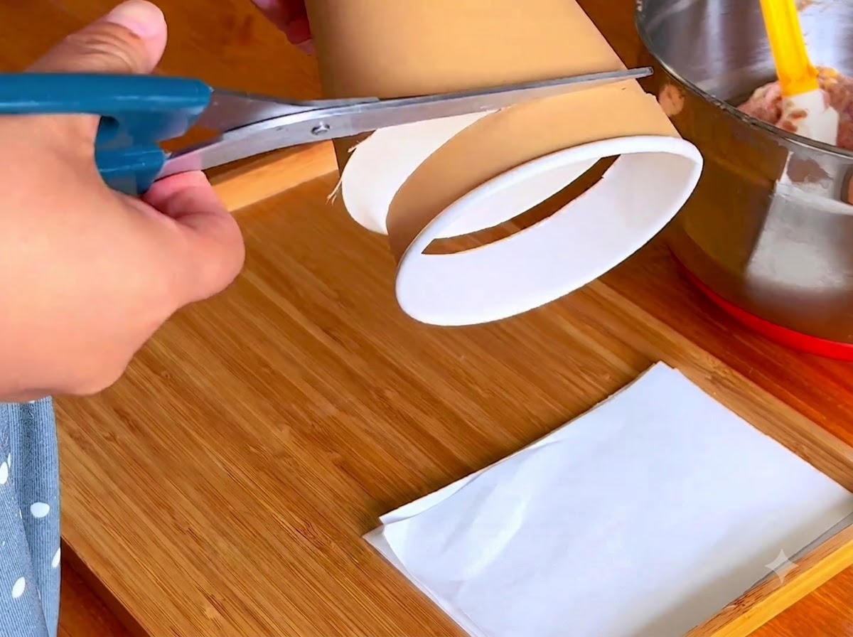 A pair of blue scissors cutting the bottom rim of a paper cup on a wooden board.