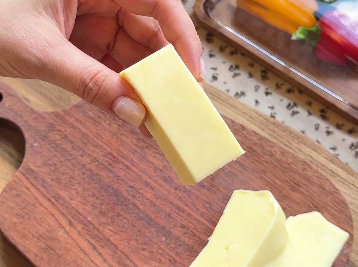 A close-up of a hand holding a rectangular block of mozzarella cheese being prepared for stuffing.