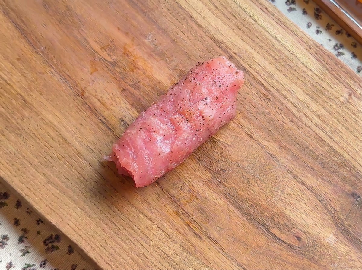 A rolled piece of seasoned pork cutlet resting on a wooden board.
