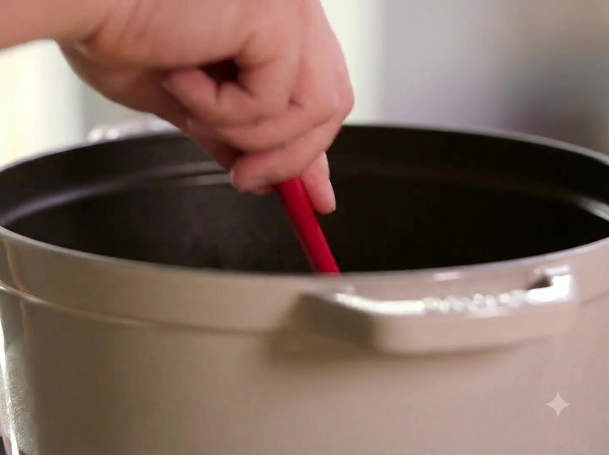 A red spatula stirring sliced onions in a cooking pot.