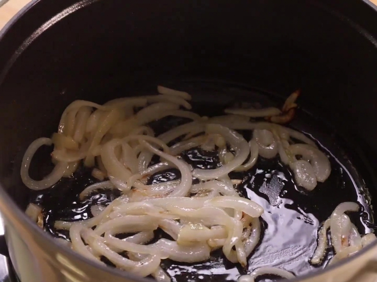 Onions sautéing in oil inside the bottom of a dark cooking pot.