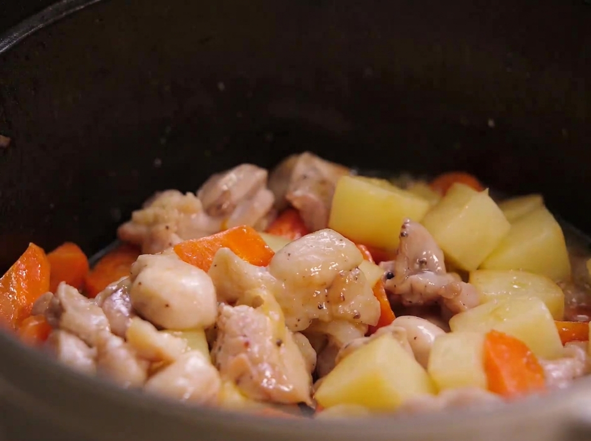 Pan-fried chicken pieces, potato chunks, and carrot pieces mixed together inside a stew pot.