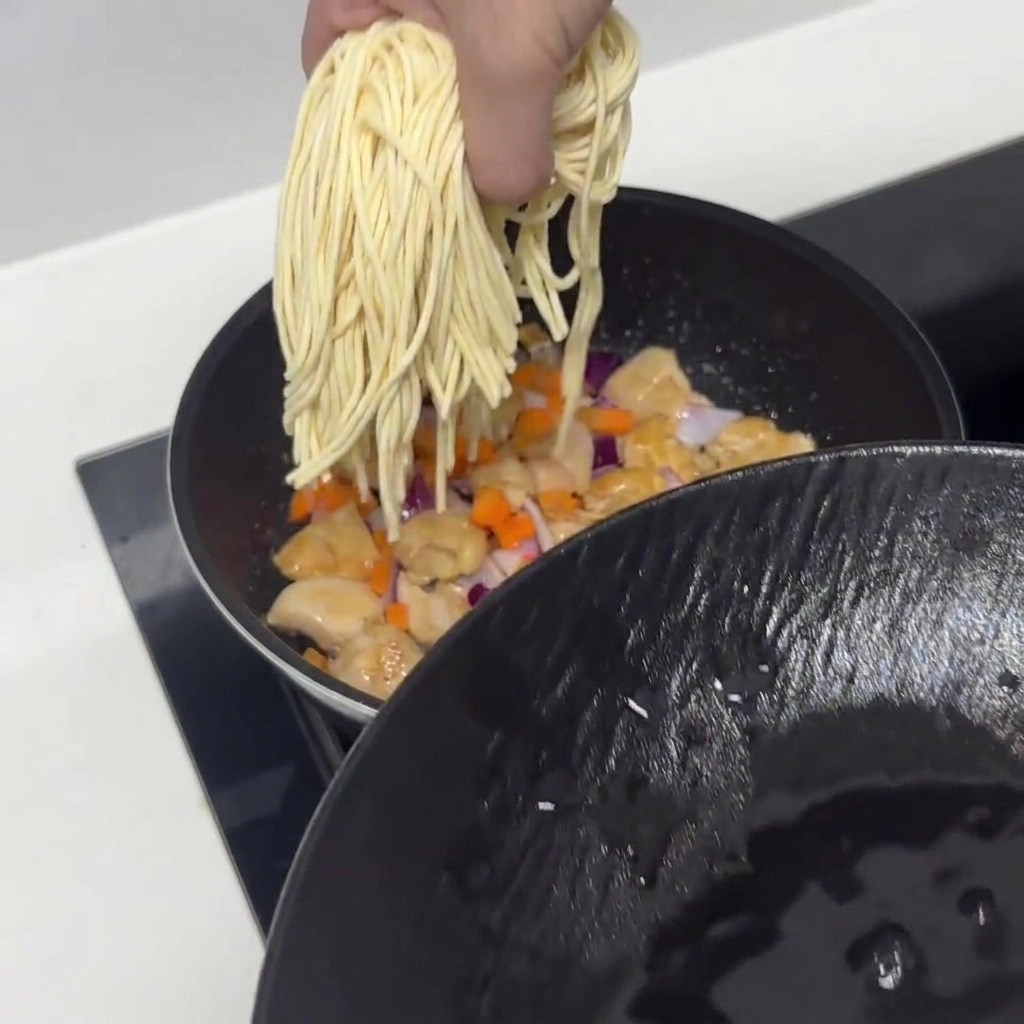 Pre-soaked pasta noodles being added into the pan with chicken and vegetables.