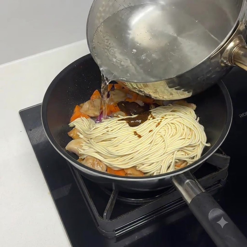 Boiled water being poured into the pan over the pasta and ingredients.